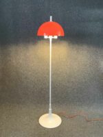 Stehlampe mit orangem, halbkugelförmigem Schirm und weißem Standfuß, ausgestattet mit drei Leuchtmitteln, verbunden über ein oranges Kabel.