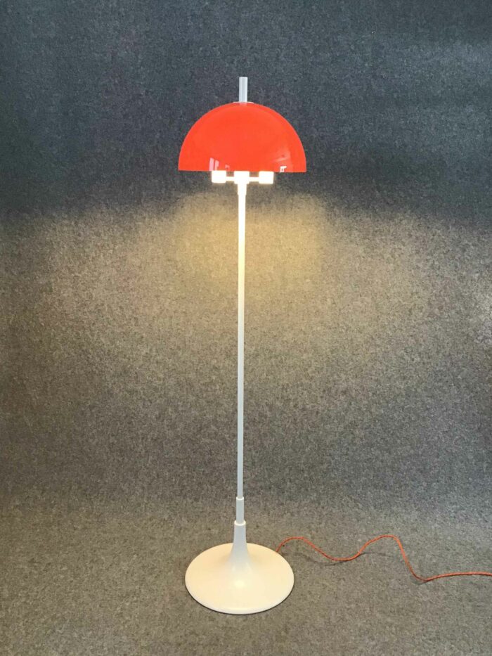 Stehlampe mit orangem, halbkugelförmigem Schirm und weißem Standfuß, ausgestattet mit drei Leuchtmitteln, verbunden über ein oranges Kabel.