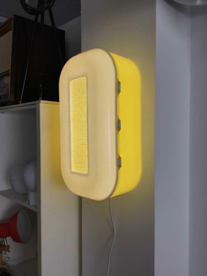 Wandlampe im Retro-Stil mit einem leuchtend gelben Gehäuse und einem rechteckigen Lichtfenster. Das Design erinnert an die 70er-Jahre und bringt Vintage-Charme in jeden Raum