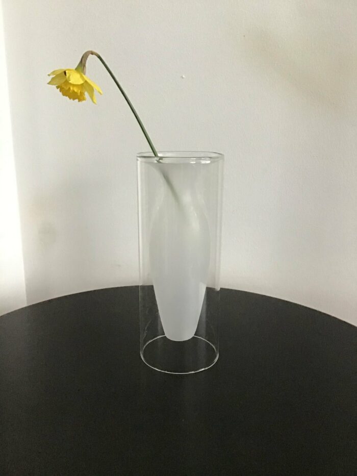 Glasvase mit elegant geschwungener Form, in der eine einzelne gelbe Blume stilvoll arrangiert ist