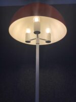 Nahaufnahme der Stehlampe mit drei sichtbaren Leuchtmitteln unter einem roten Schirm, die warmes Licht abgeben