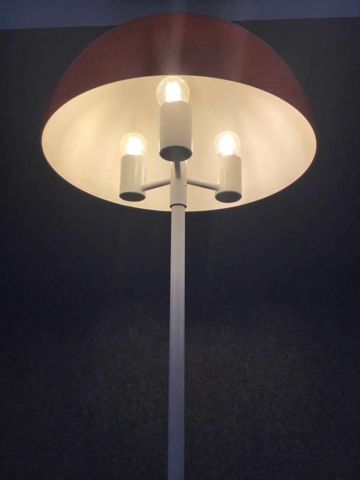 Nahaufnahme der Stehlampe mit drei sichtbaren Leuchtmitteln unter einem roten Schirm, die warmes Licht abgeben