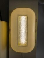Nahaufnahme einer eingeschalteten Retro-Wandlampe in Gelb mit strukturiertem Glasfenster, das warmes Licht durchlässt