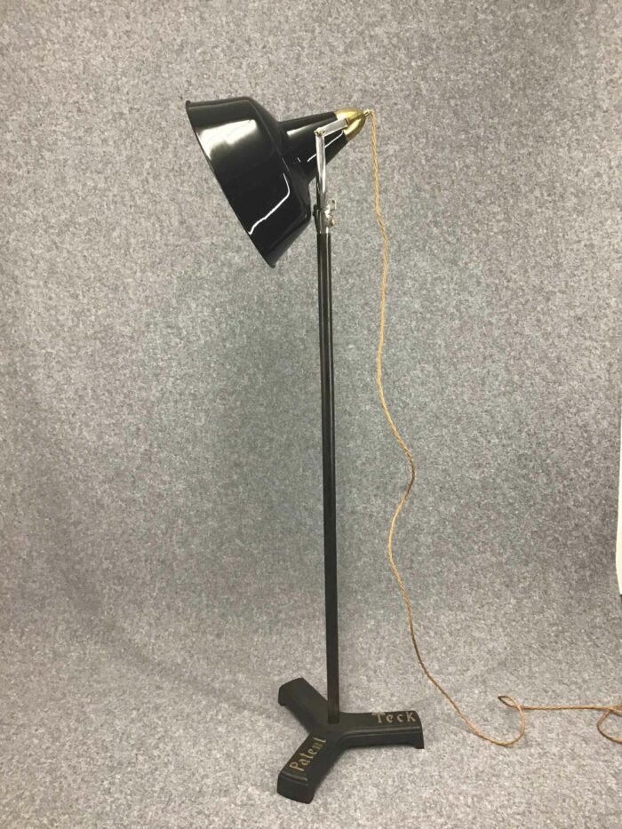 Komplette Ansicht einer Stehlampe mit schwarzem Schirm, schlankem Standfuß und dreibeinigem Fuß mit der Aufschrift „Patent Teck“.