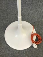 Detailansicht des weißen Standfußes der Stehlampe mit aufgerolltem orangem Kabel und Stecker