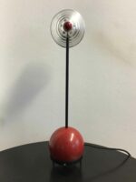 Frontale Ansicht der Tischlampe mit rundem roten Sockel und vertikalem, silbernen Lampenschirm