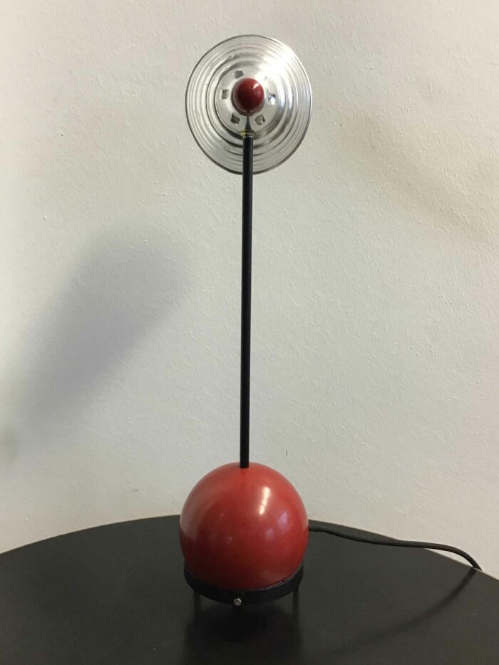 Frontale Ansicht der Tischlampe mit rundem roten Sockel und vertikalem, silbernen Lampenschirm