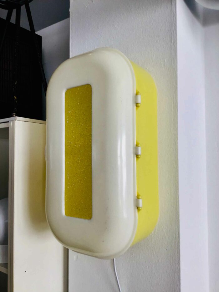 Vintage-Wandlampe mit gelbem und weißem Kunststoffgehäuse, montiert an einer Wand