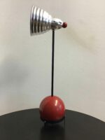 Lampenschirm in glänzendem Silber auf einem schwarzen Ständer, mit einem roten, kugelförmigen Sockel