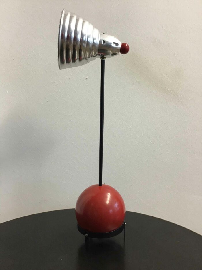 Lampenschirm in glänzendem Silber auf einem schwarzen Ständer, mit einem roten, kugelförmigen Sockel
