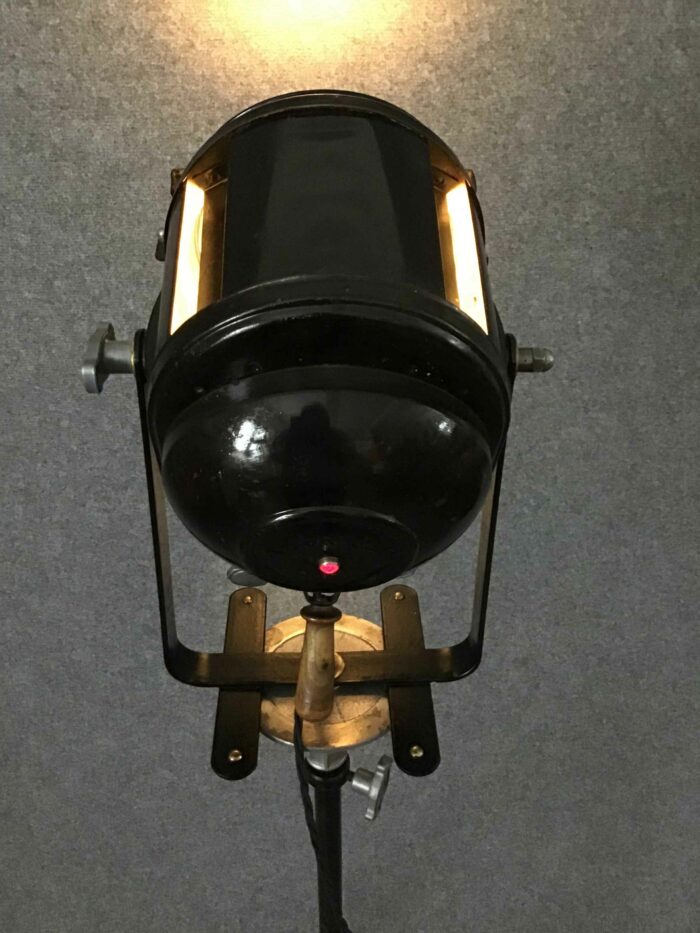 Rückansicht eines schwarzen Studioscheinwerfers auf Stativ mit einem roten Kontrolllicht und stabiler Metallkonstruktion.